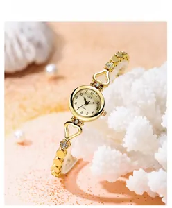 Close-up of golden GEDI watch with heart-shaped bracelet links on white coral decor