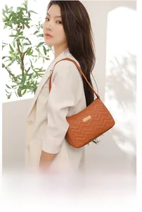 Detail of caramel quilted leather shoulder bag with chic wavy embroidery and metal plaque