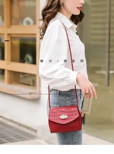 Close-up of red crocodile embossed saddle bag with elegant pearl twist lock and gold hardware