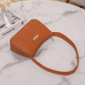 Brown V-quilted faux leather underarm bag with gold metallic detail on marble surface