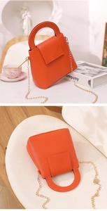 Gros plan du mini sac à main orange vif avec bandoulière en chaîne dorée sur table