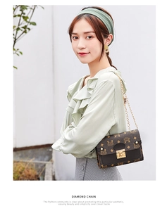 Detail of dark brown leather crossbody bag with vintage pattern and gold chain strap