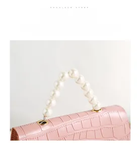 Detail der rosa Kroko-Handtasche mit weißem Perlengriff und goldenen Metallteilen