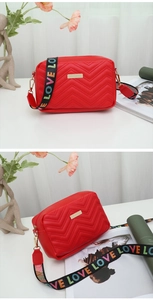 Detail view of red quilted crossbody bag with golden hardware and rainbow LOVE strap