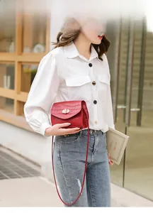 Detail of red crocodile pattern crossbody bag with a golden flower lock on a model