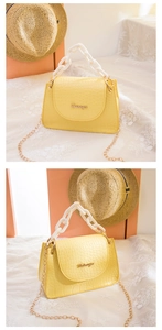 Detailansicht der gelben Handtasche mit Krokoprägung, Goldlogo und Acryl-Tragekette