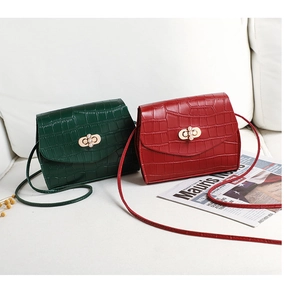 Close-up of crocodile pattern bags in green and red with pearl clasps on white sofa