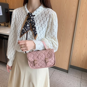 Pink quilted crossbody bag with dual buckles and top handle worn with a lace blouse