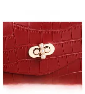 Detail of red croc-embossed leather handbag featuring a gold clasp with three pearls