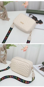 Detail of cream quilted camera bag with V-shaped stitching and colorful LOVE strap