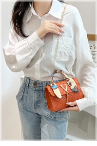 Detail of orange quilted crossbody bag with tassel, silk scarf handle and gold chain strap