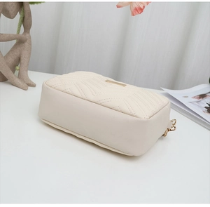 Detail of cream chevron quilted crossbody bag with elegant gold metal logo plate
