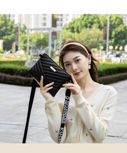 Détail d'un sac bandoulière noir matelassé avec boucle dorée et large sangle tissée