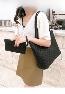 Model showcasing a large black quilted tote bag and matching clutch in a modern setting
