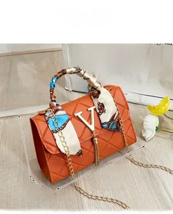 Detail of orange quilted crossbody bag with gold V-logo, tassel, and silk scarf handle