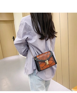 Detail of snake pattern crossbody bag with gold lock and chain strap on model