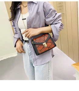 Model wearing a small orange snakeskin crossbody bag with a gold metal clasp and chain