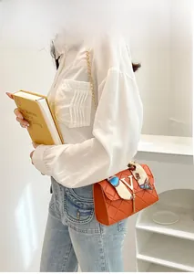 Detail of orange quilted crossbody bag with metal V logo, tassel and printed silk scarf