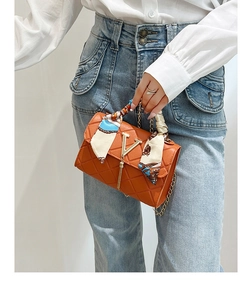 Detail of orange quilted handbag with gold V-clasp and decorative silk scarf on handle