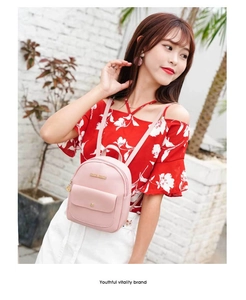 Detailed view of a light pink mini PU leather backpack with a gold logo and front flap