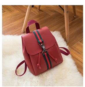 Detail of red PU backpack with striped web ribbon and metal hook on soft white fur