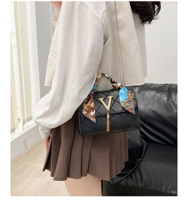 Detail of black quilted crossbody bag with golden V logo, tassel, and silk scarf handle