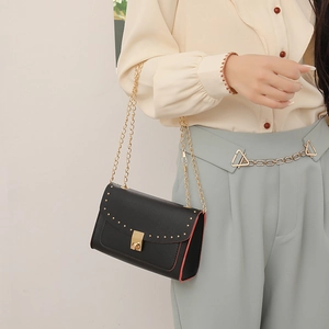 Elegant black leather crossbody bag with gold rivets, chain strap and red edge details