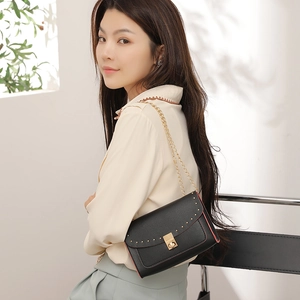 Chic black leather crossbody bag with gold studs and chain strap shown on a model