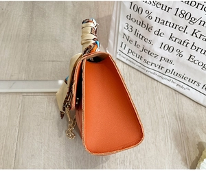 Detail of orange faux leather mini bag featuring silk scarf handle and gold chain hardware