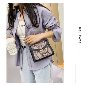 Detail of snake print pattern on crossbody bag with gold twist lock and chain strap