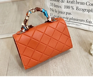 Detail of orange quilted handbag featuring a silk scarf wrapped handle and gold hardware
