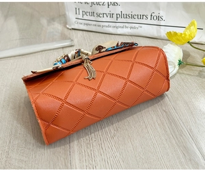 Detail view of orange quilted PU leather mini bag with silk scarf handle and golden tassel