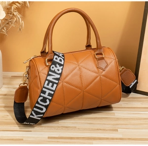 Gros plan du sac cylindrique matelassé marron avec zips dorés et large bandoulière tissée