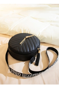 Close-up of black round quilted shoulder bag with dual tassels and lettered woven strap