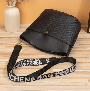 Detail of black bucket bag with V-quilted leather and branded contrast strap