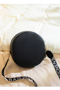 Close-up of black round shoulder bag with embroidered wide strap on white background