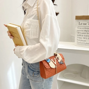 Orange quilted crossbody bag with gold chain strap and decorative silk scarf detail