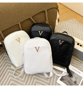 Detail view of crocodile-embossed and smooth leather backpacks with gold V-shape hardware