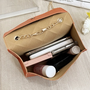 Orange crossbody flap bag with gold chain showing interior space for phone and makeup