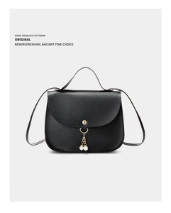 Detail view of black textured leather bag with round gold buckle and pearl tassels