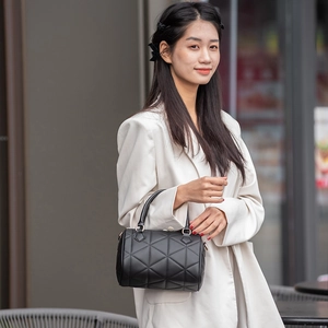 Sac Boston noir matelassé élégant avec coutures géométriques et poignées rondes porté par un mannequin