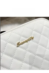 Detail of white quilted camera bag with gold logo and elegant rhombus stitching