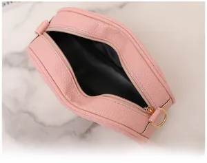 Gros plan du sac rond en cuir rose montrant le grain de galet et les boucles dorées