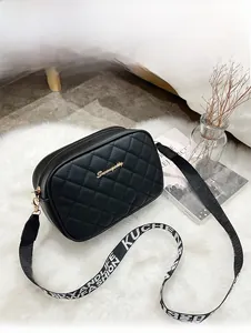 Detail of black quilted crossbody bag with golden logo on white plush carpet