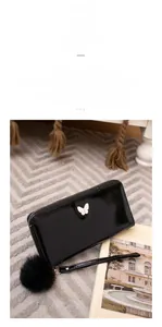 Close-up of glossy black long wallet with gold butterfly logo and black pompom charm