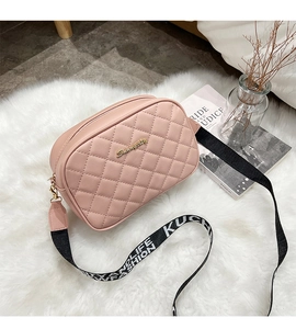 Detail of pink quilted camera bag with adjustable lettered strap on a soft white rug