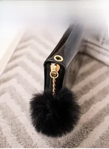 Detail of black patent leather wallet with gold zipper and fluffy fur ball keychain