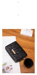Detailed view of black quilted coin purse with gold metal trim and faux fur pompom charm