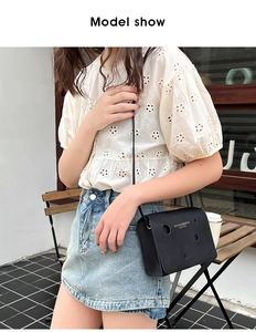 Detail of black leather crossbody bag with circular hole design worn by a female model