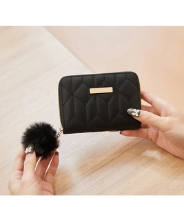 Detail of a black quilted coin purse with a gold metal plate and soft pompom charm